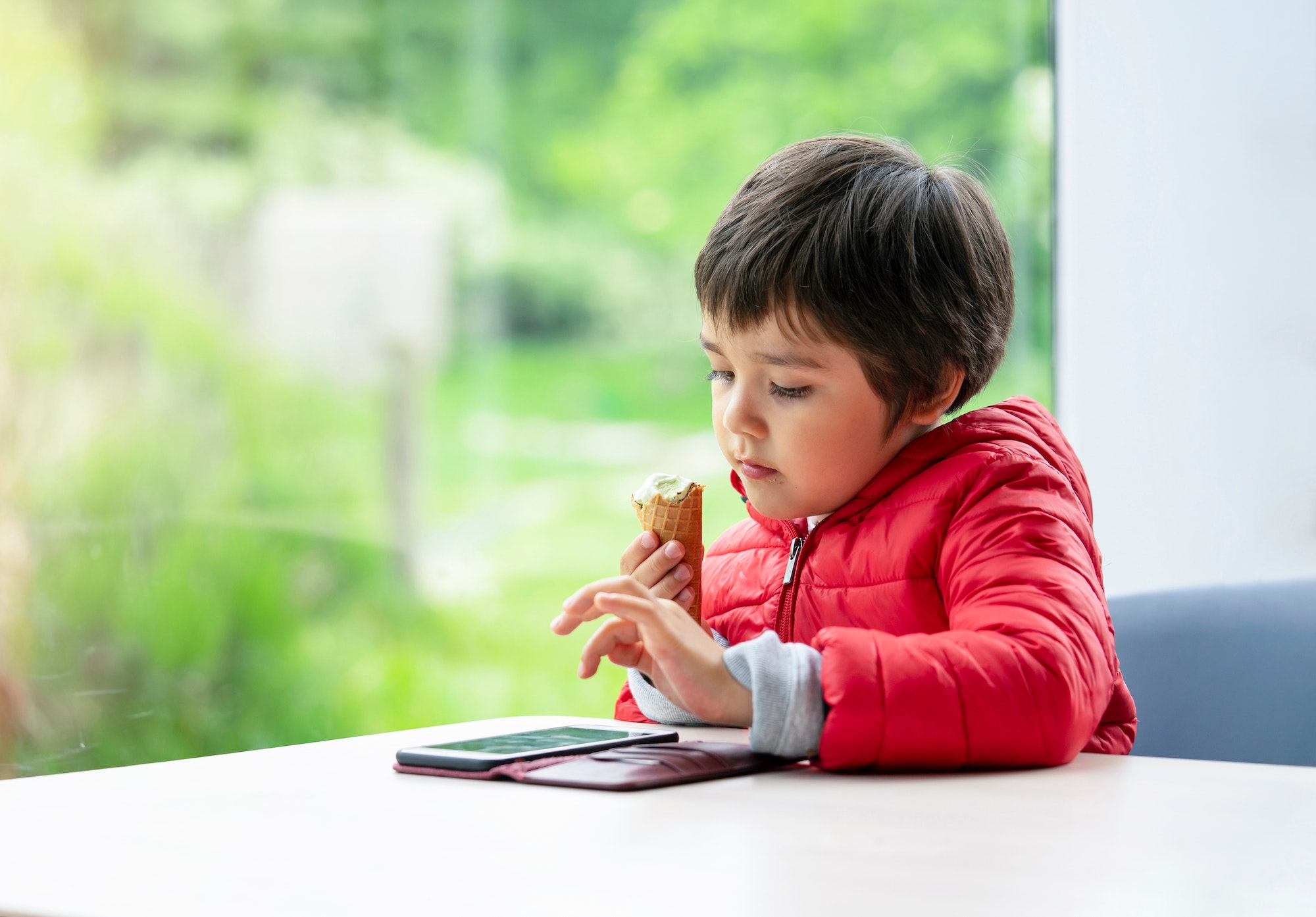 Kid eating ice cream, young boy watching cartoon or playing game on Mobil phone